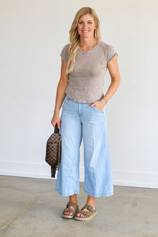 Woman wearing a gray t-shirt and light blue jeans, holding a handbag.