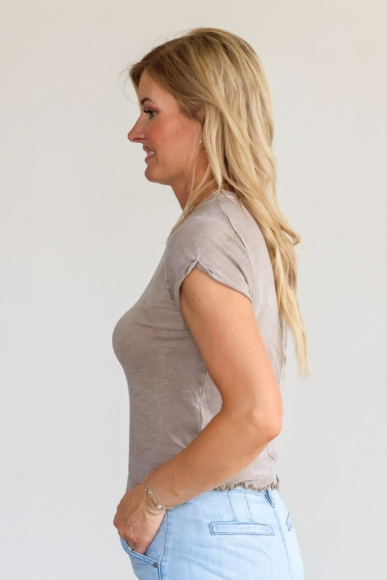 Woman wearing a gray top and light blue pants standing against a white wall.