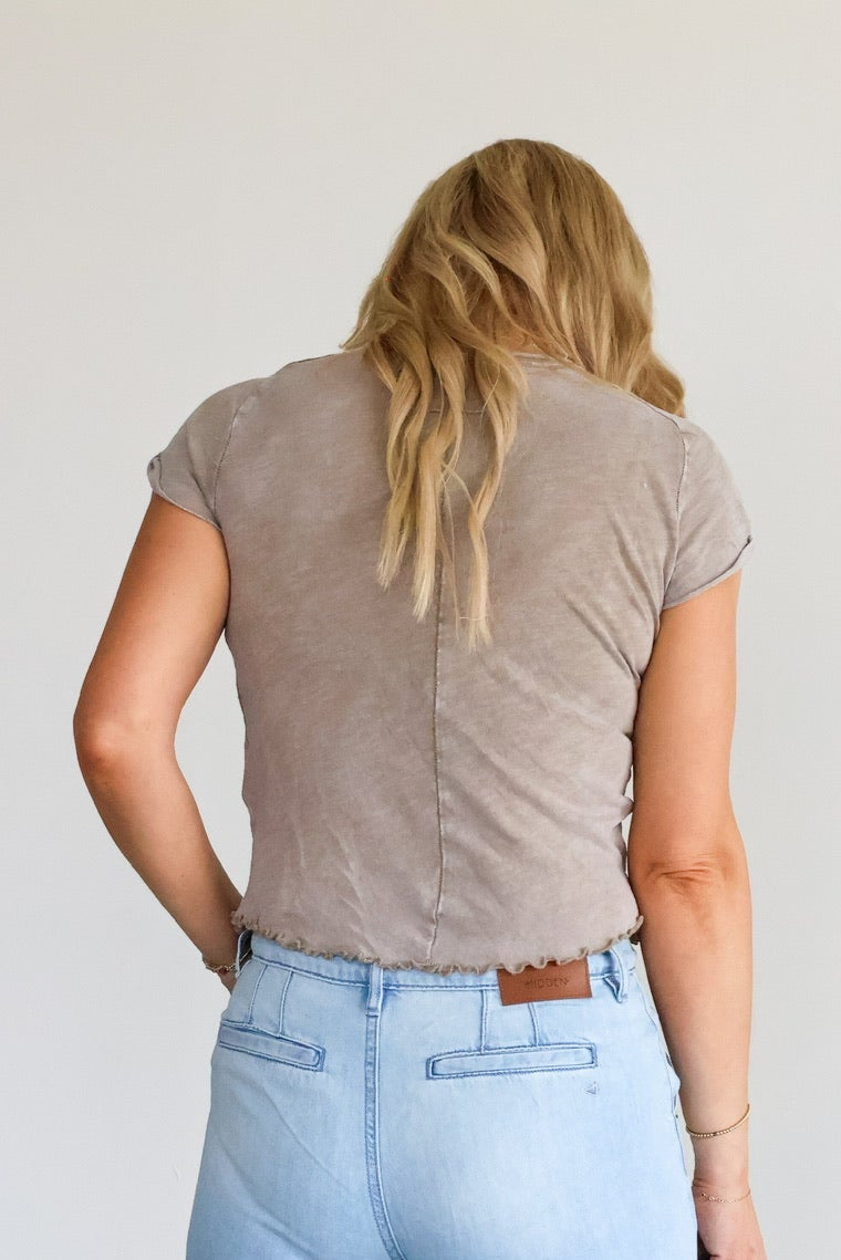Person wearing light blue jeans and a brown shirt, standing against a white wall.