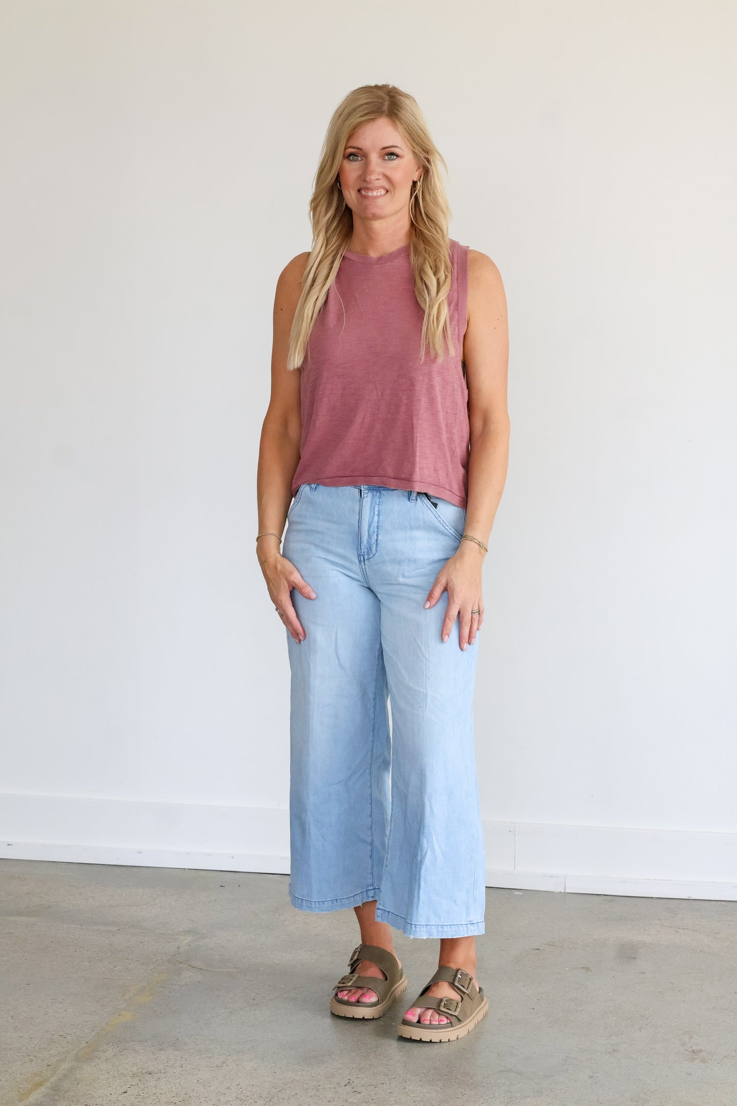 Woman wearing a pink sleeveless top and light blue jeans against a white background